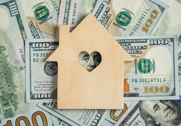 Selling to Cash House Buyer - A model of a wooden house on background of cash representing cash for houses in Austin, TX