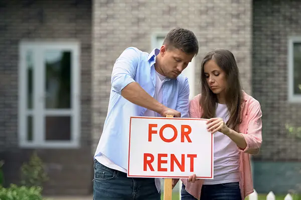 Landlords standing in front of a rental home in Austin, TX with a For Rent sign — Austin House Buyer purchases tenant-occupied properties and duplexes for cash.