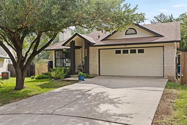 Front view of a single-family home in Austin, TX with a two-car garage and shaded driveway, representing houses bought for cash by Austin House Buyer.